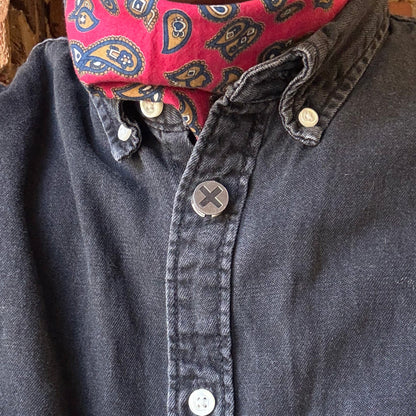 Person wearing a dark denim shirt with a red patterned collar against a brick wall.